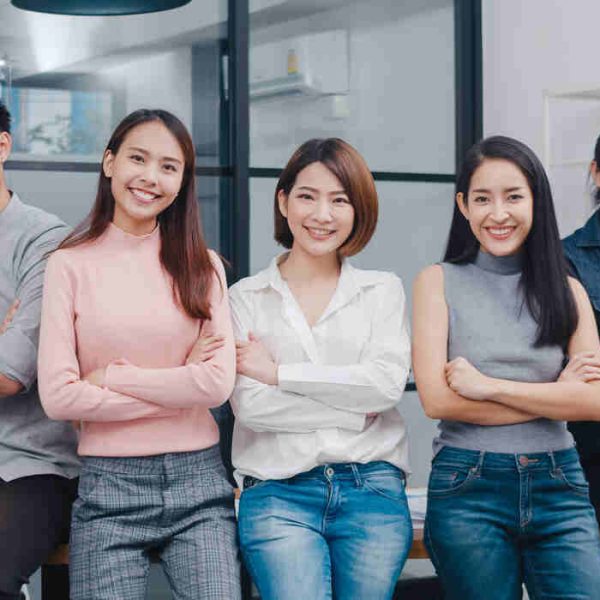 Group of Asia young creative people in smart casual wear smiling and arms crossed in creative office workplace. Diverse Asian male and female stand together at startup. Coworker teamwork concept.